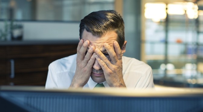 Stressed man with head in hands in front of computer